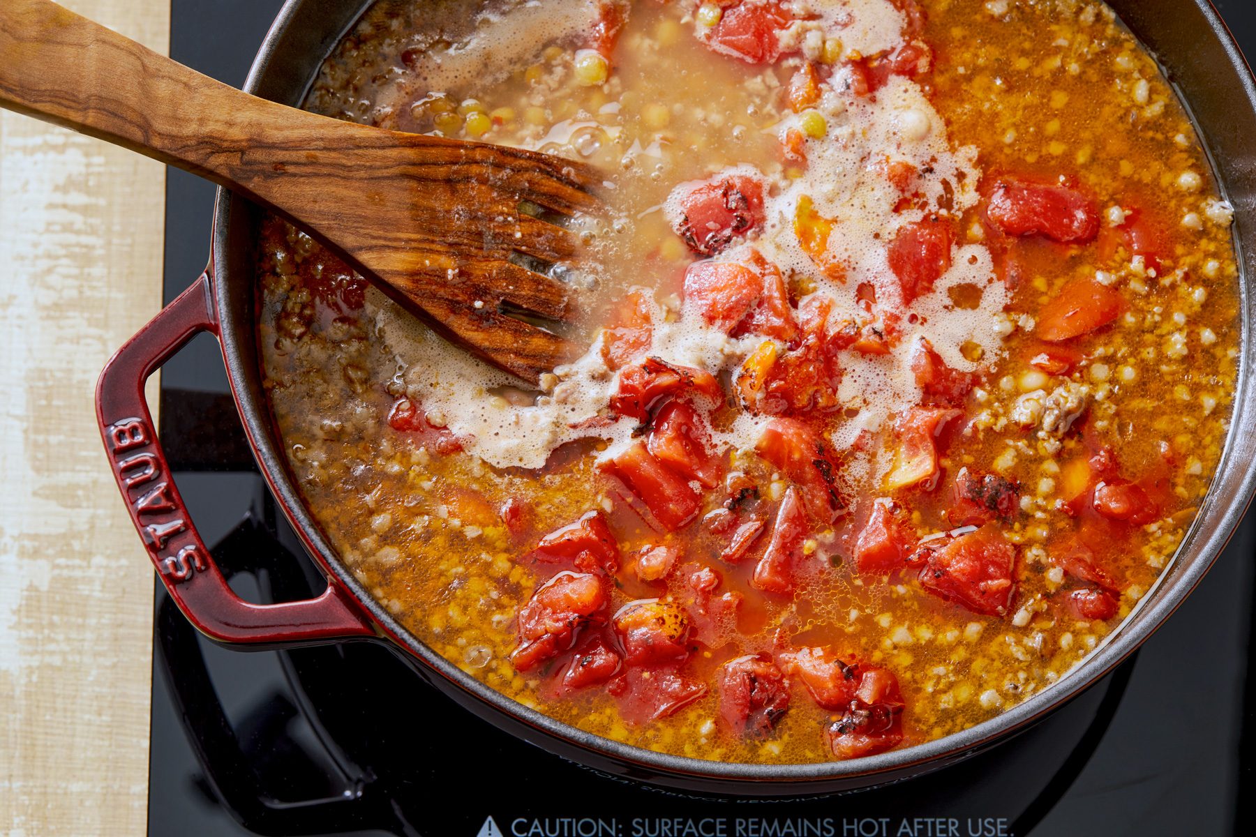 overhead shot; added tomatoes in the pan, a wooden spatula rests in the pan