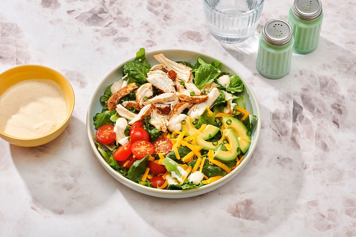Chicken taco salad assembled on a serving plate with extra salad dressing on the side