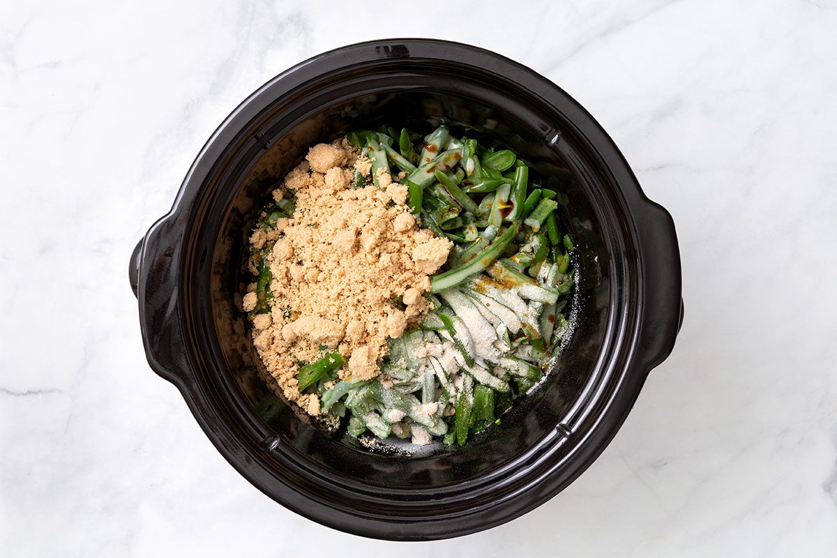 Green beans with melted butter, brown sugar, garlic salt and soy sauce in a slow cooker for step two of Slow Cooker Green Bean recipe for Taste of Home