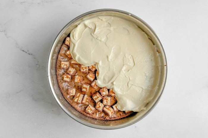 Batter for Taste of Home Snickers Cheesecake in a springform pan on a marble surface