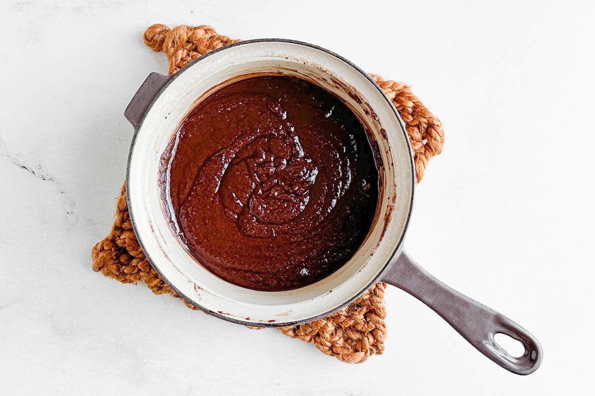 Batter for brownie layer of Taste of Home Snickers Cheesecake in a ceramic saucepan on a marble surface