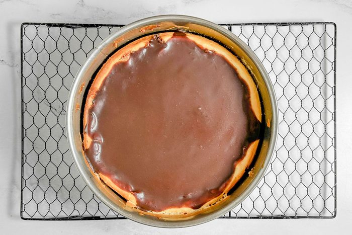 Taste of Home Snickers Cheesecake in a springform pan on a wire rack on a marble surface