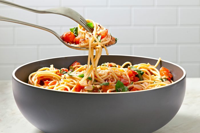Table view shot of Spaghetti Pomodoro; serve with Parmesan cheese; and top with additional fresh basil and crushed red pepper flakes; fork; spoon; marble surface