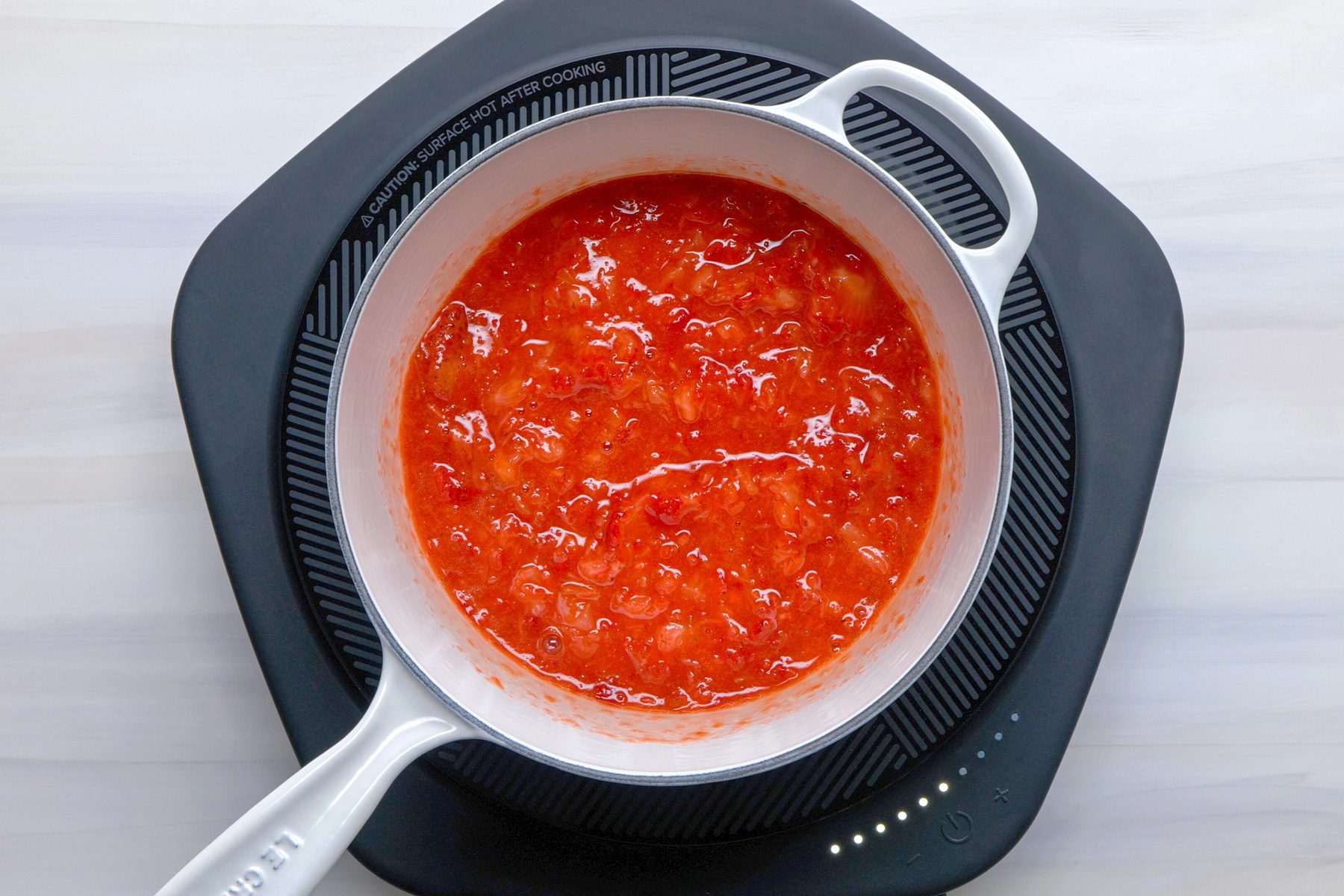Overhead shot of measure 4-1/2 cups berries into a large saucepan; stir in pectin and bring to a rolling boil over high heat; stirring frequently; induction; wooden surface