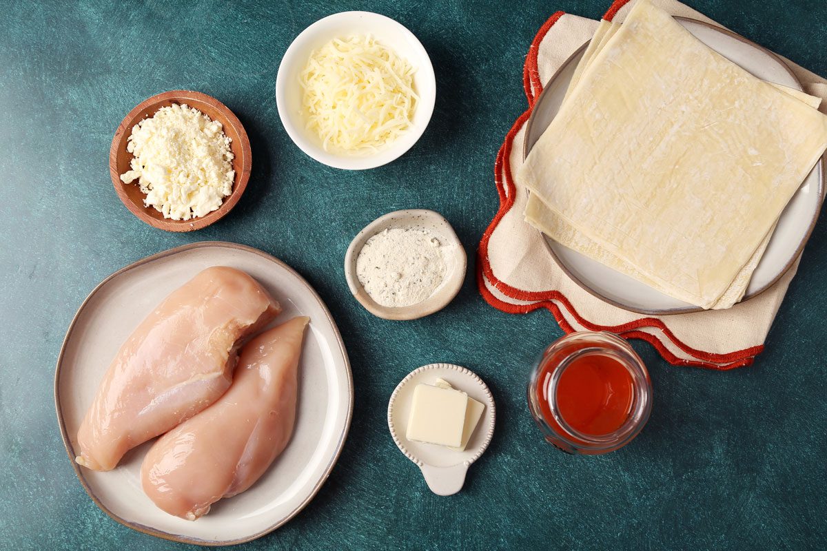 Ingredients for Taste of Home's Buffalo Chicken Egg Rolls out in small bowls on a green surface.