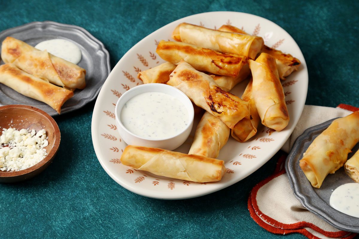 Close up of Taste of Home's Buffalo Chicken Egg Rolls on a serving dish on a green board.