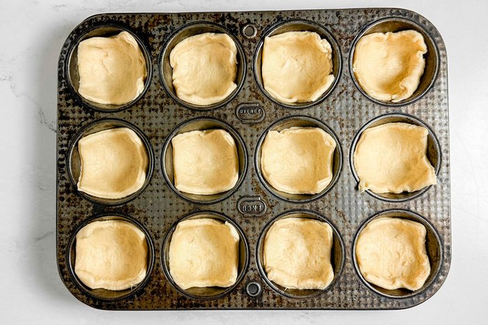 Crescent roll squares for Taste of Home Taco Cups in a vintage muffin tin on a marble surface