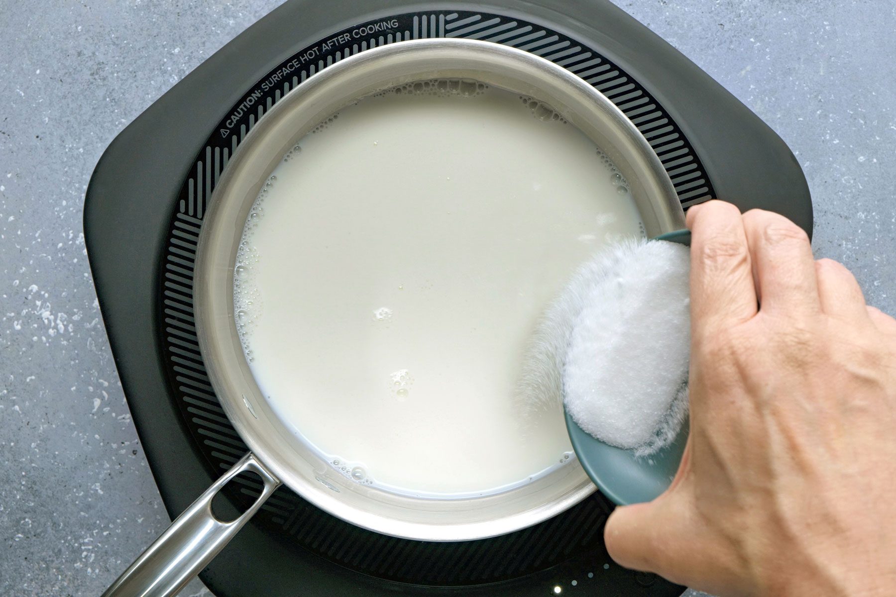 Sugar being sprinkled on heated milk.
