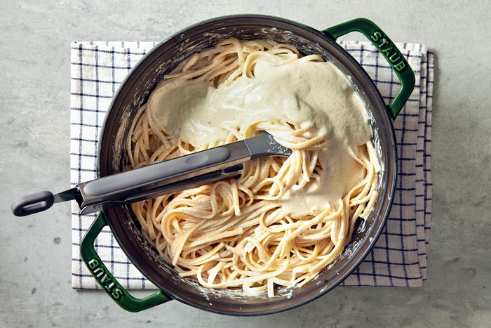 Overhead shot of cook linguine according to package directions; reserve 2 cups pasta water; drain the remaining pasta water; place pasta back in pot; add sauce to pot with pasta; toss to combine;tongs; kitchen towel; grey marble surface