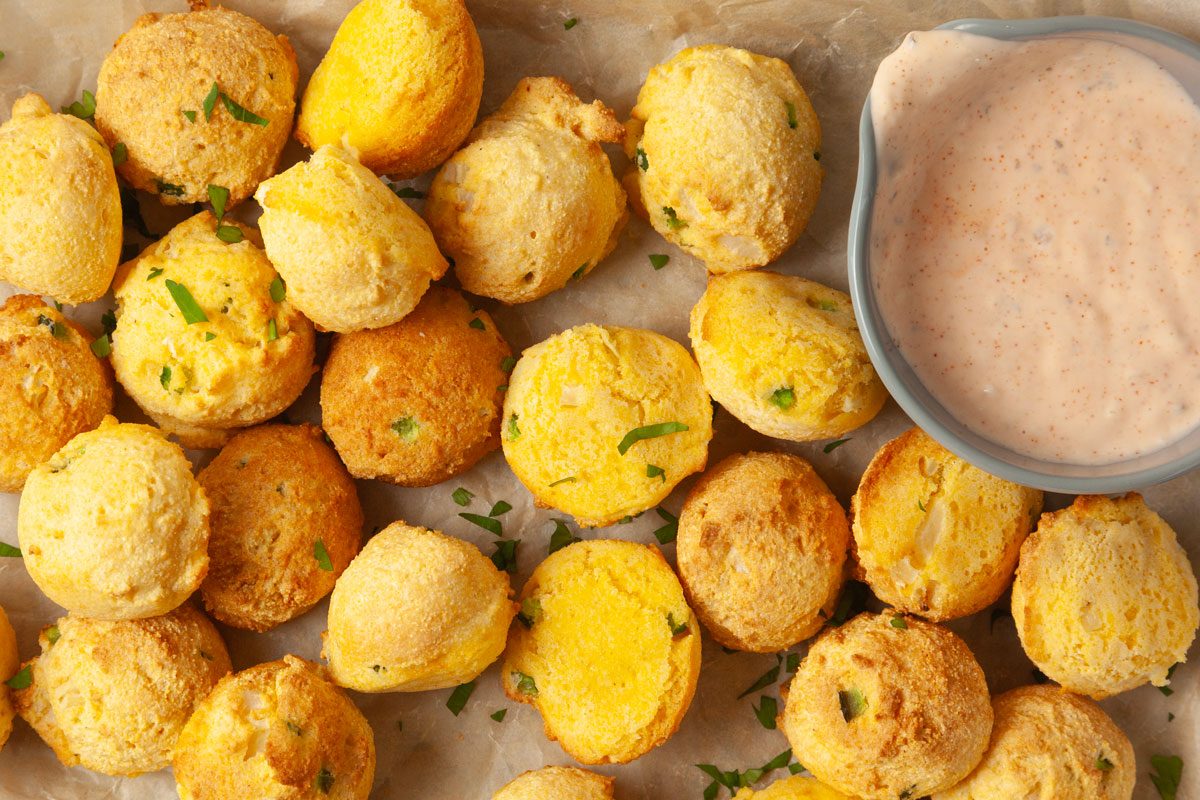 Close up of Taste of Home Air-Fryer Hush Puppies on a metal tray lined with parchment paper, remoulade dipping sauce