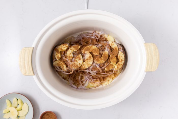 Pork loin on slow cooker topped with red onions, apple slices and cinnamon.