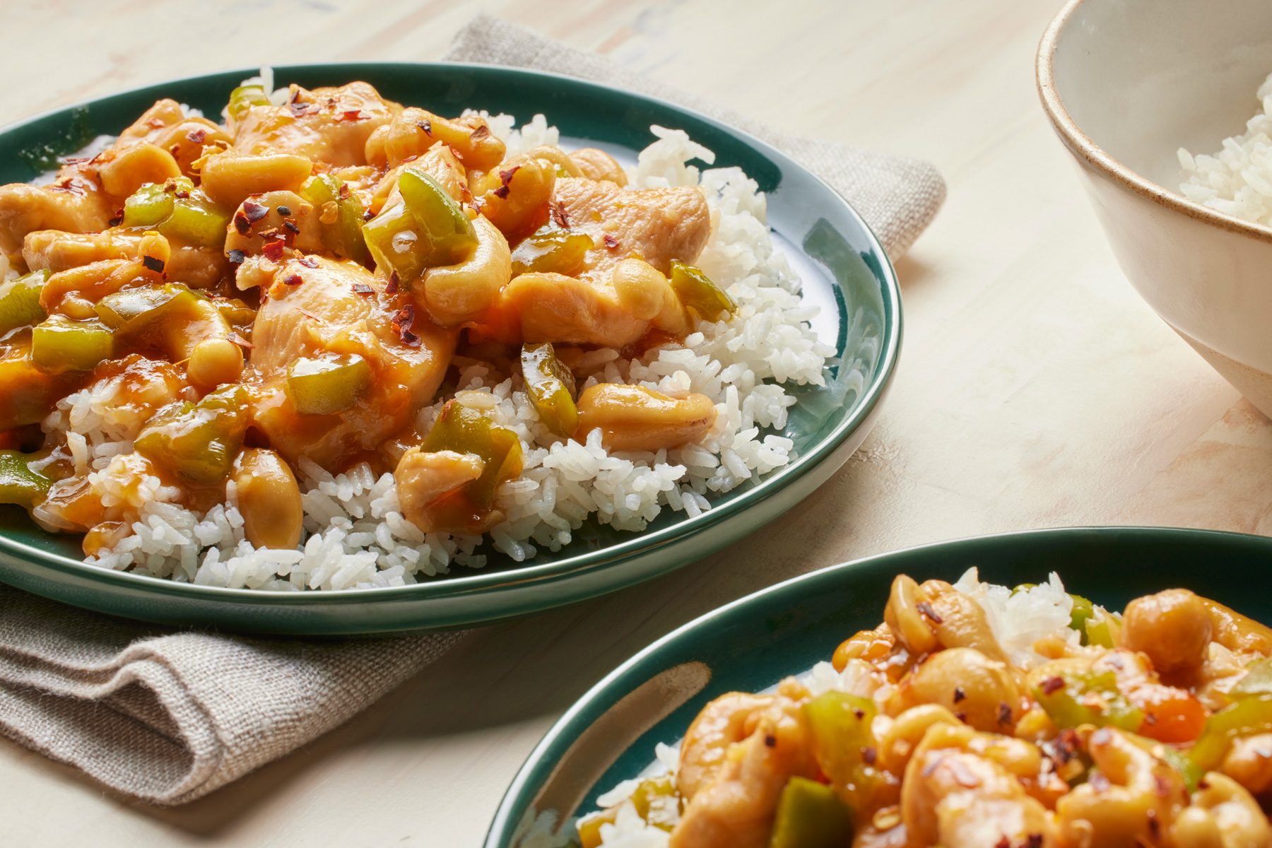 3/4th shot of a dish called Apricot Chicken placed over wooden background, The dish consists of stir-fried chicken coated in a sweet and tangy apricot sauce, The chicken is served over a bed of white rice and garnished with red pepper flakes, The dish is accompanied by a bowl of steamed rice
