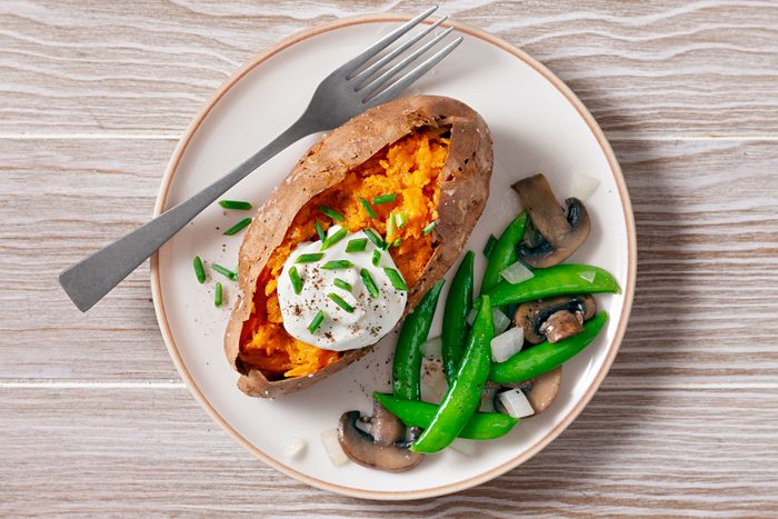 Baked Sweet Potato served with beans and mushrooms on a white plate.