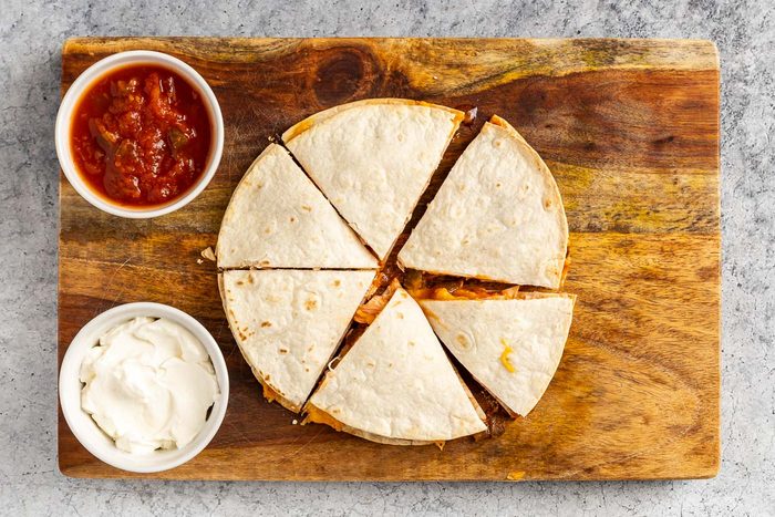 Bbq Chicken Quesadilla on a cutting board with salsa and sour cream on the side