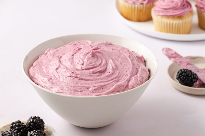 Close up of blackberry buttercream in bowl, with frosted cupcakes in the background.