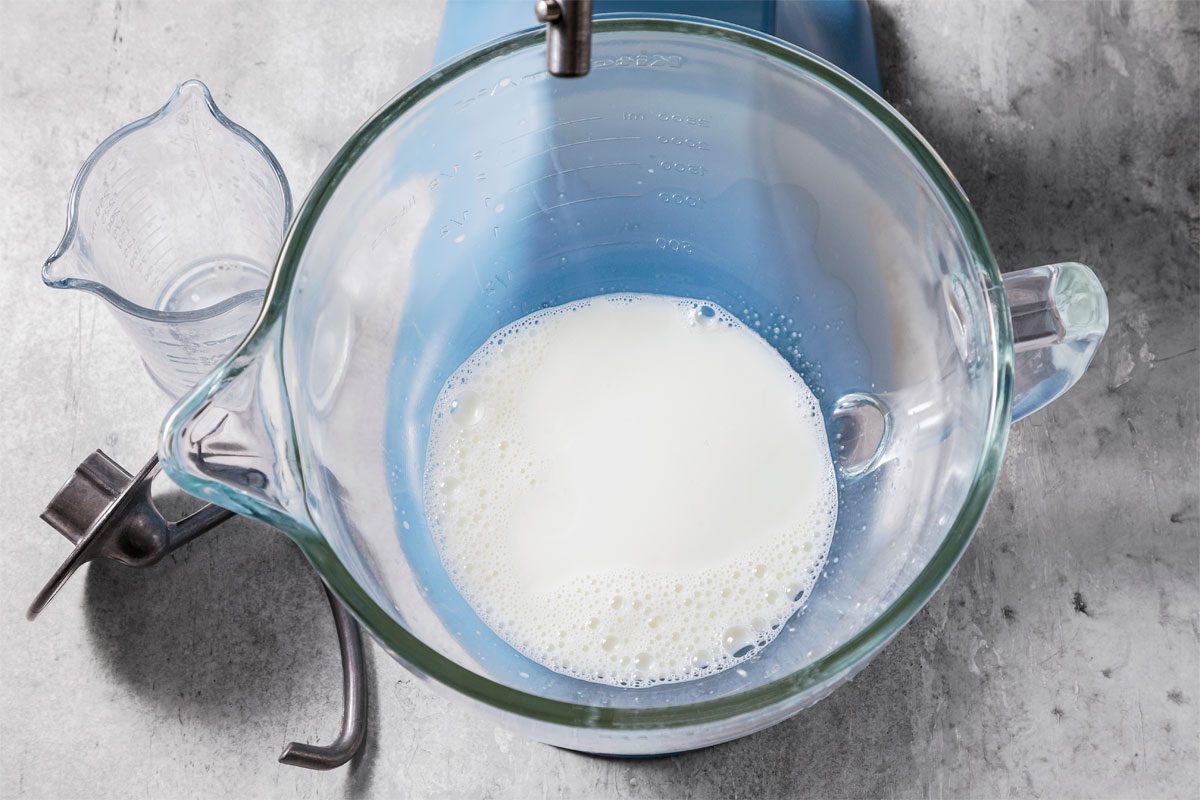 milk and sugar in a mixing bowl with hook attachment nearby
