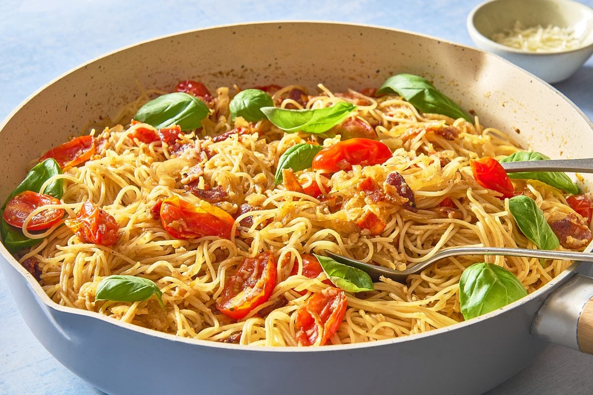 Closeup shot of caramelised onion pasta in a skillet being served with utensils