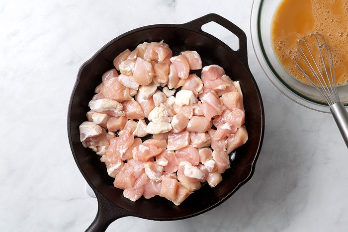 Large cast iron skillet heating chopped chicken breast next to a bowl of soy sauce mixture for step one of Cashew Chicken recipe for Taste of Home