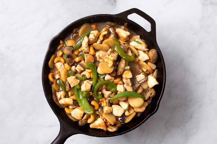 Chopped chicken breasts and salted cashews added to stir fry mixture in cast iron skillet for step three of Cashew Chicken recipe for Taste of Home