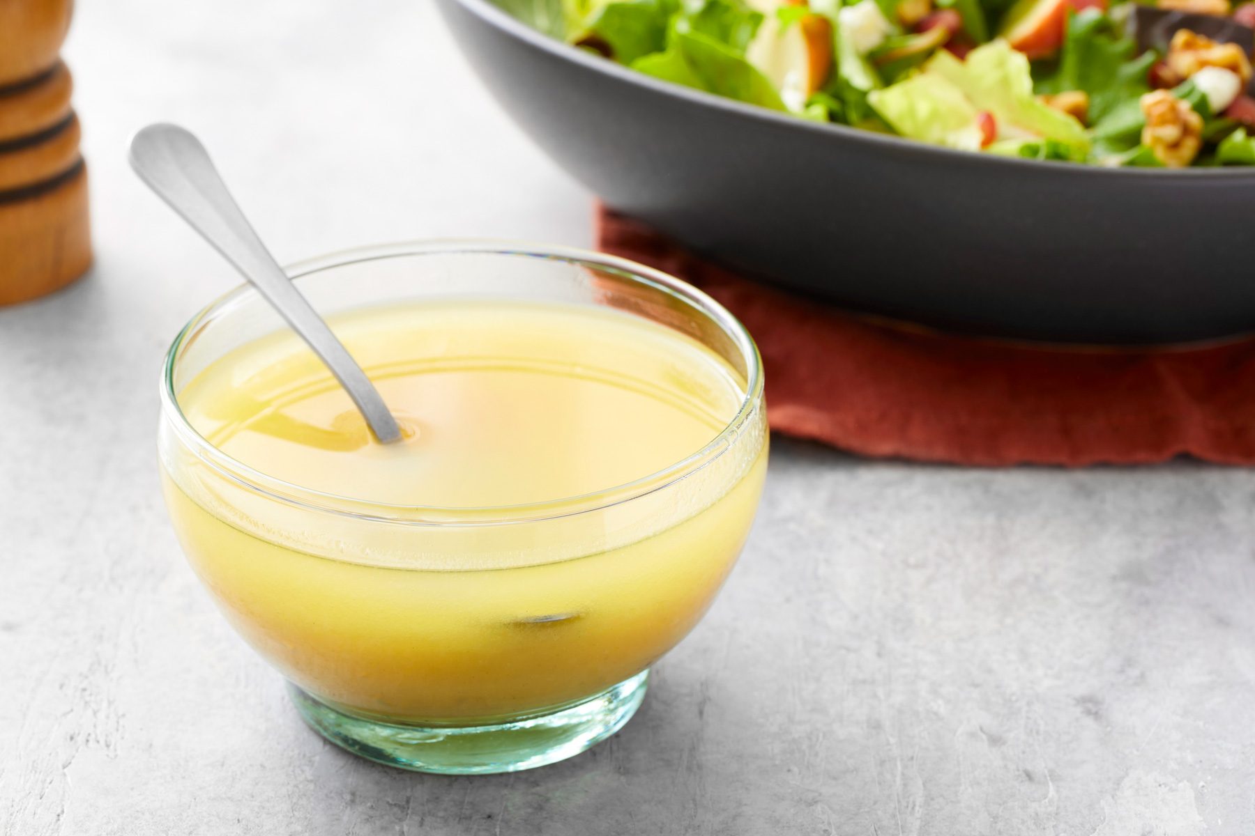Table view shot of Champagne Vinaigrette; in a glass bowl; spoon; served with salad; napkin; salt shaker; grey background;
