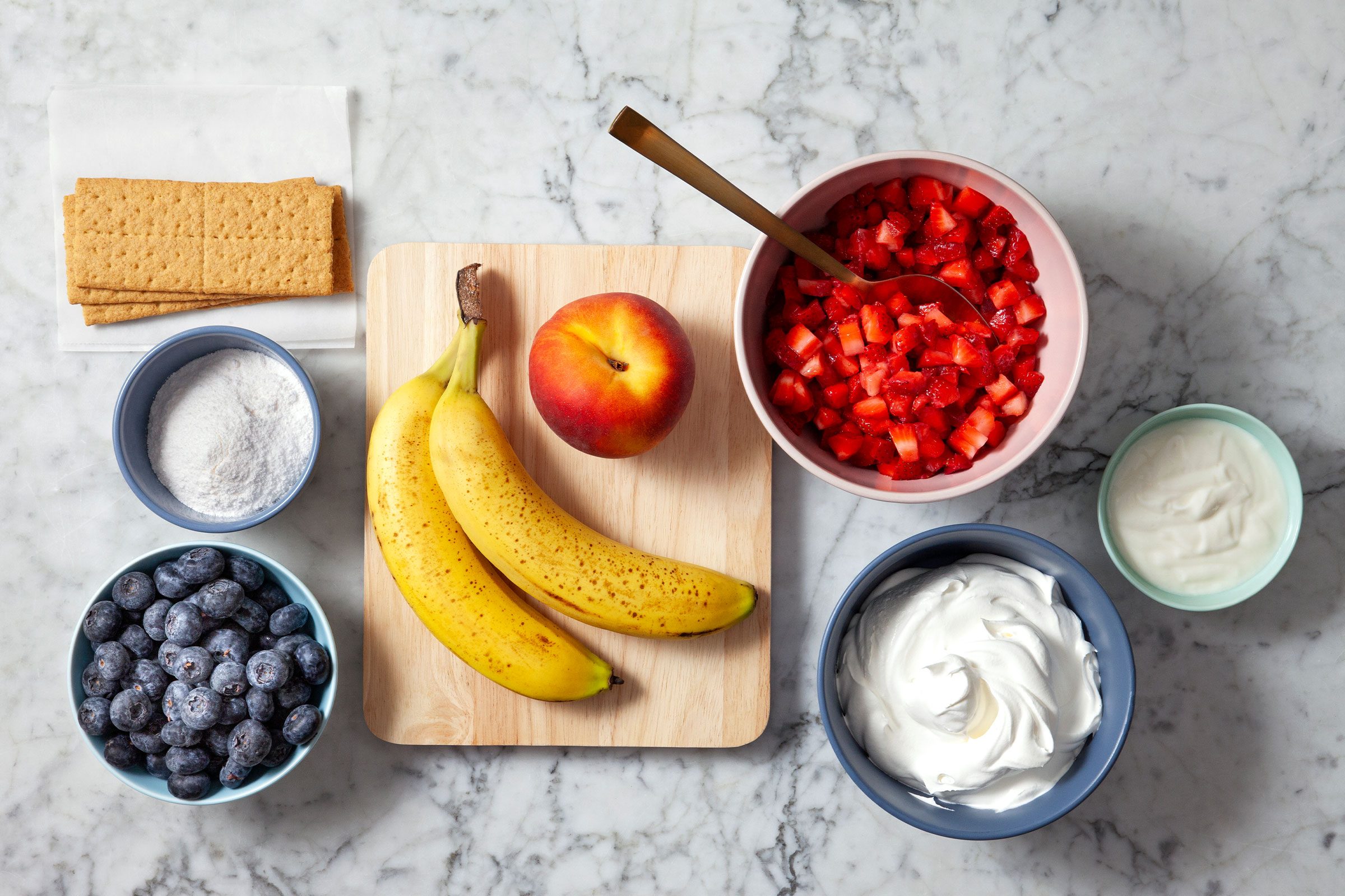 Fresh strawberries, bananas, blueberries, yogurt, apple and crackers on a surface