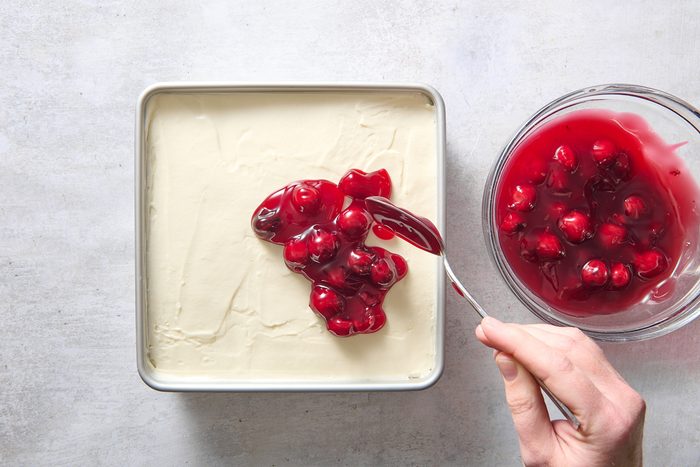 Spooning cherry filling on top of the layered dessert