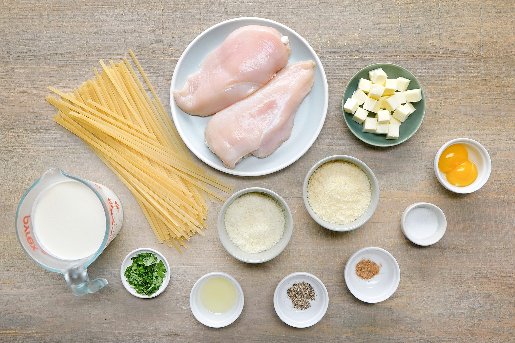 overhead shot of Chicken Alfredo ingredients placed over wooden background;