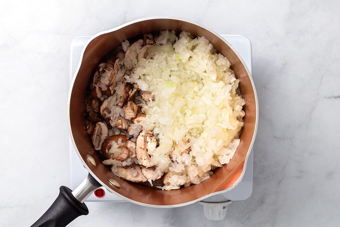 Sliced mushrooms and onion cooking in a saucepan for step two of Chicken Risotto recipe for Taste of Home