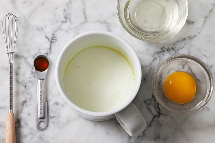 Milk and oil combined in a mug with egg yolk and vanilla extract next to it.