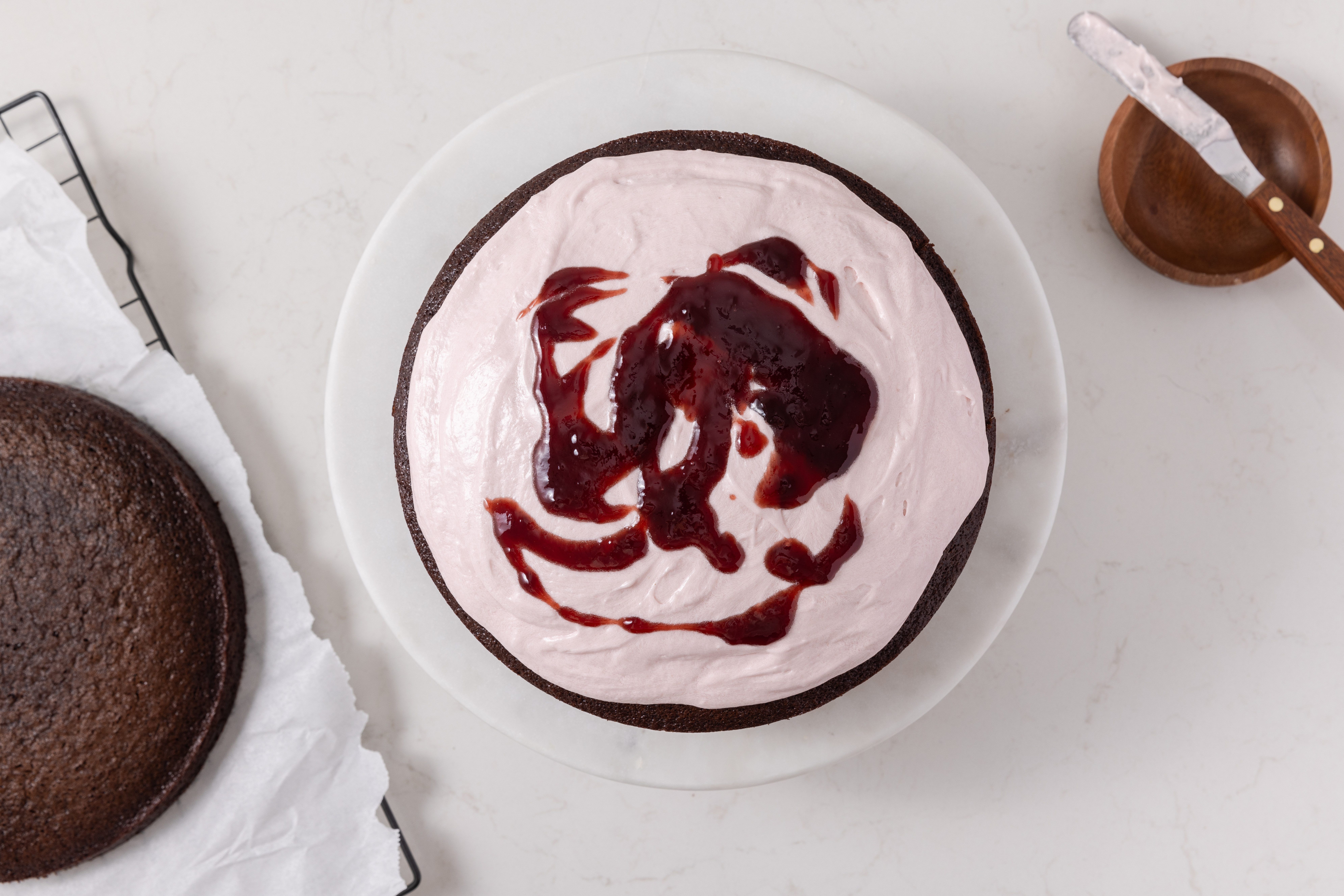 Chocolate raspberry cake being layered with filling and raspberry jam.