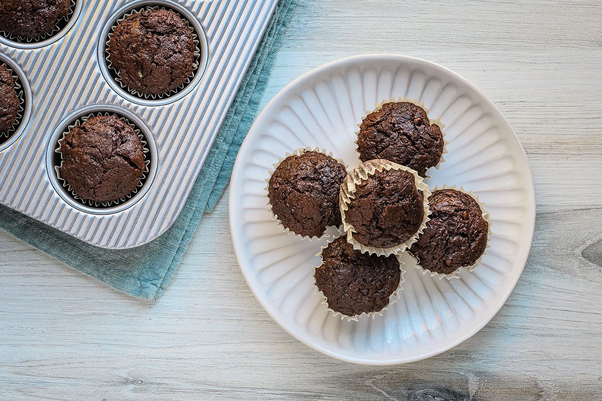 Freshly baked homemade chocolate zucchini muffins on a plate with more in a muffin tin in the background.