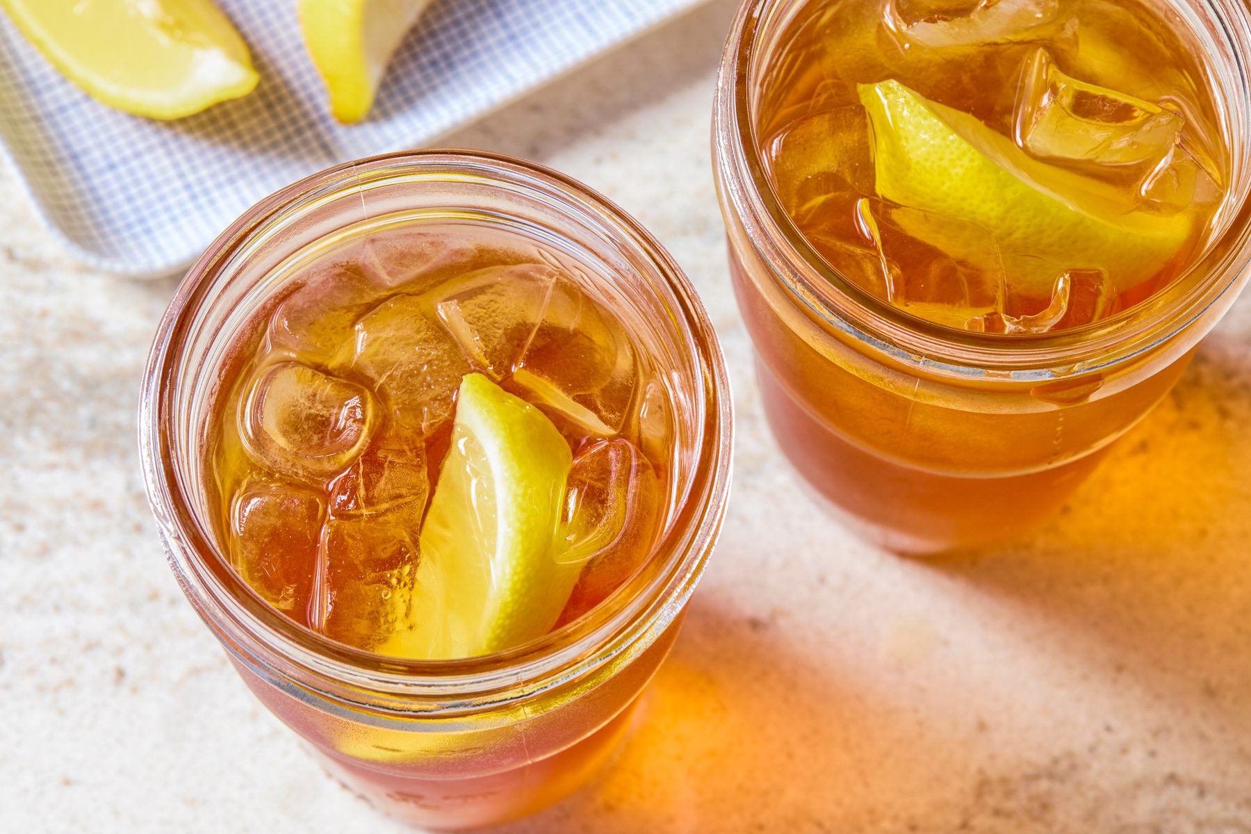 Overhead shot of two mason jars filled with light amber iced tea and lemon slices, with ice cubes clearly visible inside.
