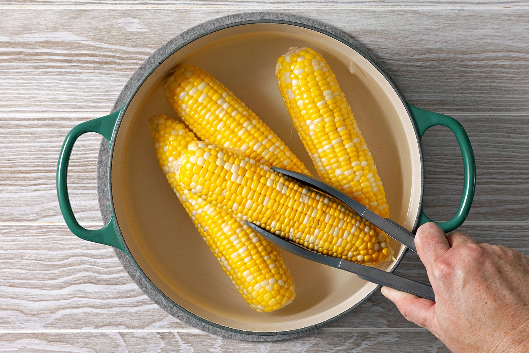 Overhead shot of a large saucepot; bring a quart of water to boil; add corn; cook for 5 minutes; tongs; wooden surface;