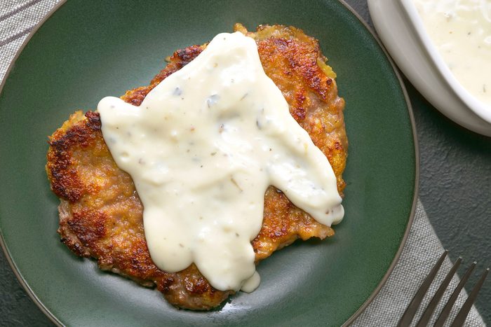 overhead shot of plate of Country-Fried Steak with White Gravy is showcased, The steak is breaded and pan-fried, resulting in a golden brown exterior and a tender interior, A generous pool of creamy white gravy covers the steak;