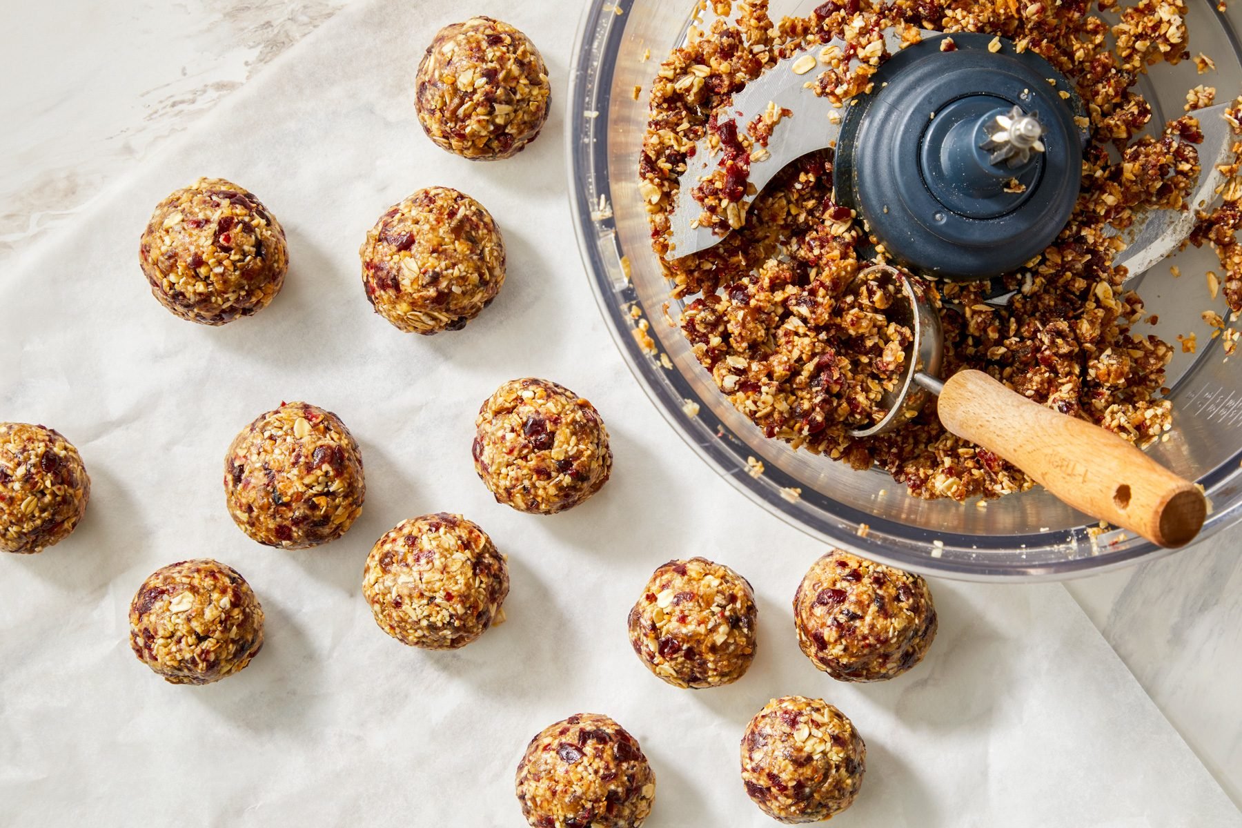 Shaping a sticky mixture into 1.5-inch balls, with several finished energy balls resting on a parchment-line.