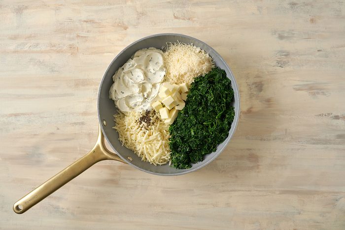 Combining spinach, cream cheese, and other ingredients in a saucepan, cooking until blended and warm for the Creamed Spinach with Cream Cheese recipe, by Taste of Home.