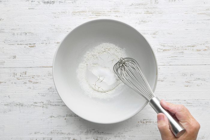 overhead shot of bowl placed white wooden background, mixing flour, sugar and salt