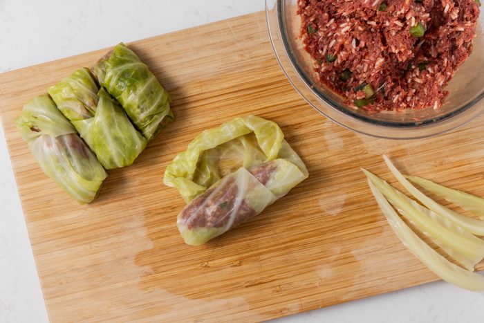 Cabbage rolls being rolled with beef mixture filling.