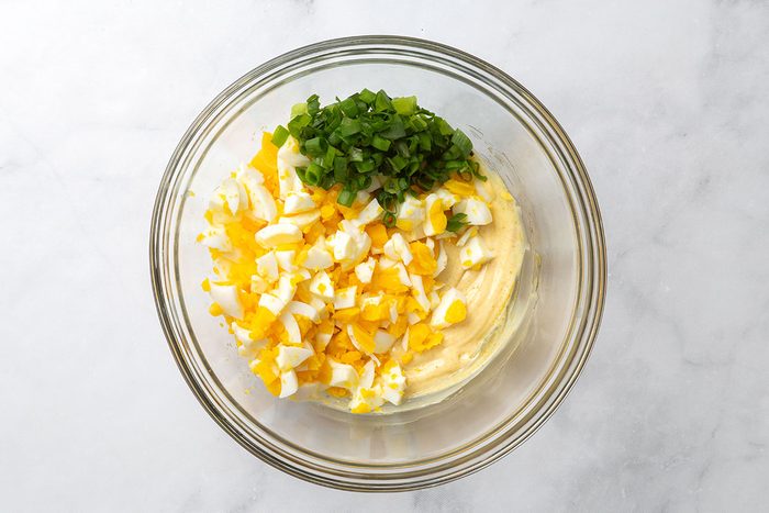 Coarsely chopped hard-boiled eggs and green onion in a mixing bowl with mayonnaise dressing for step two of Curried Egg Salad for Taste of Home