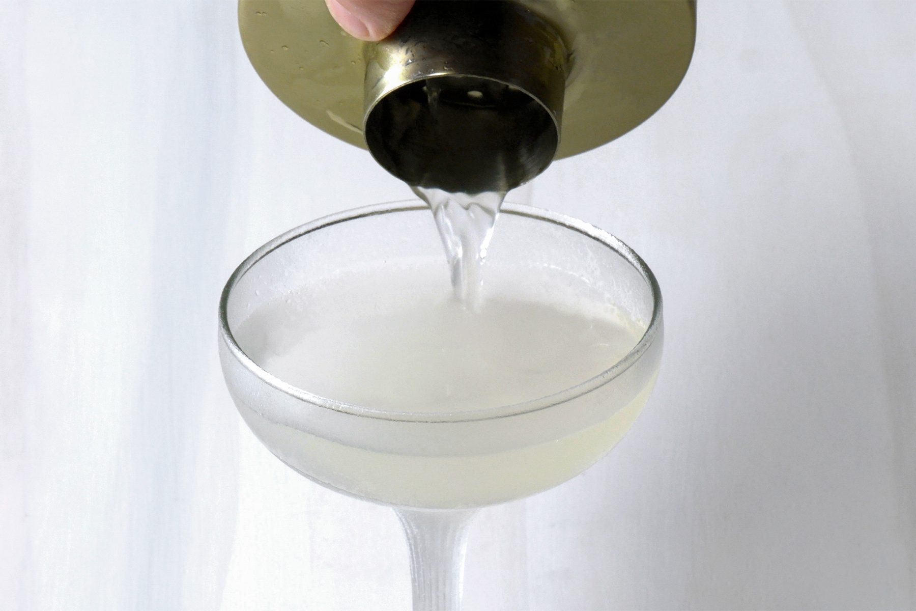 High angle view shot of strain into a chilled coupe glass; shaker; white background;
