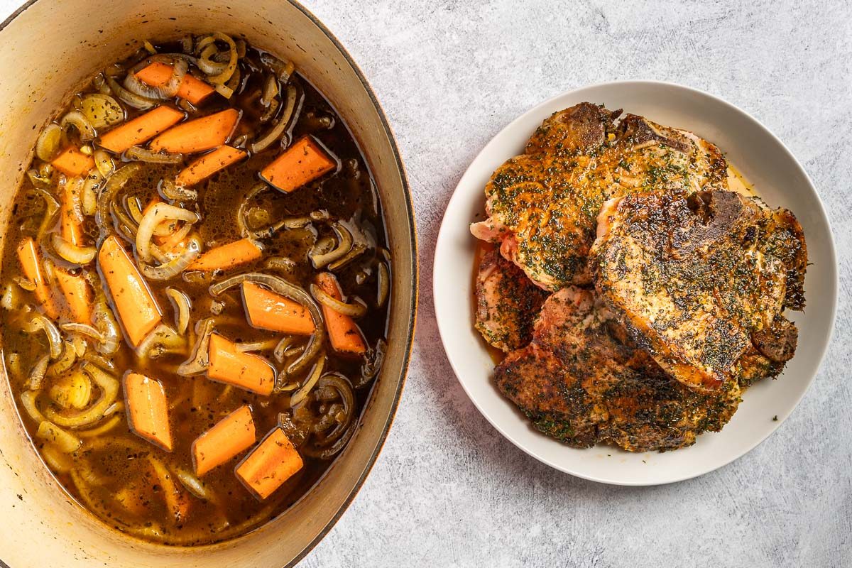 Taste of Home Dutch Oven Pork Chops photo of the seasoned and. browned pork chops with the carrots and broth in the Dutch oven.
