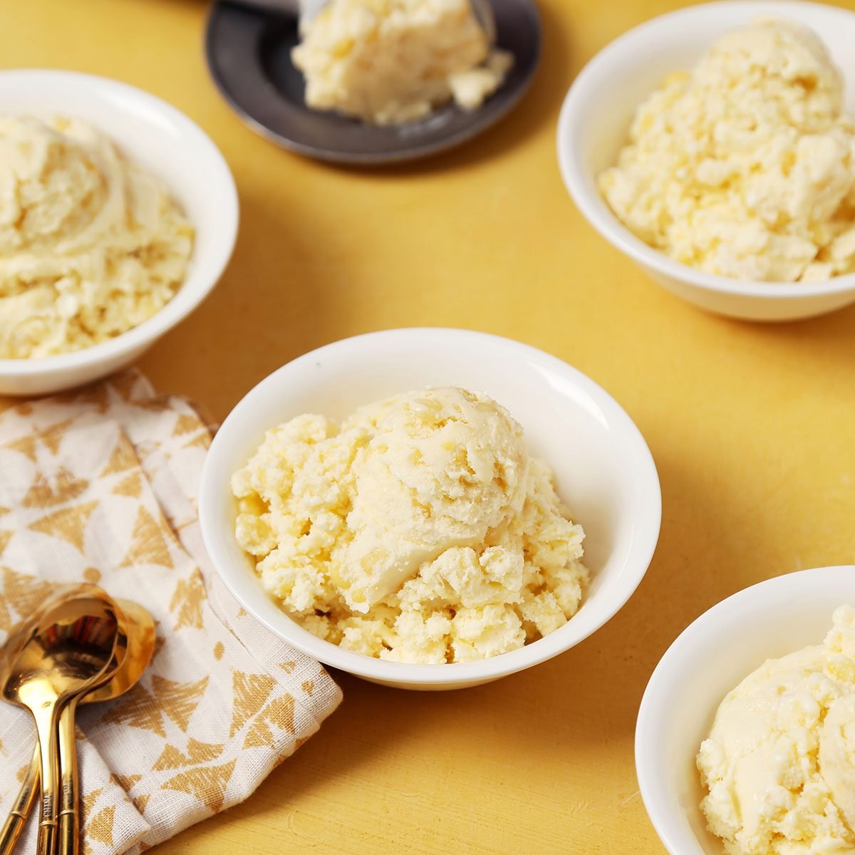 Close up of Taste of Home's Corn Ice Cream scooped and served in small white bowls on a yellow surface.