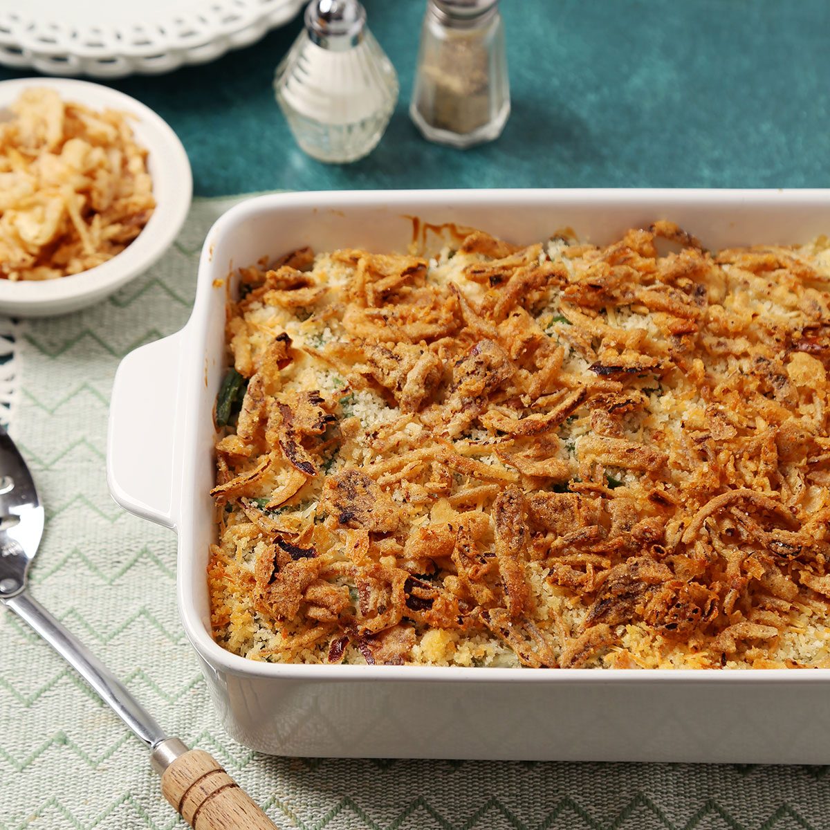Close up of Taste of Home's Gluten Free Green Bean Casserole served on white lace plates on a teal surface.