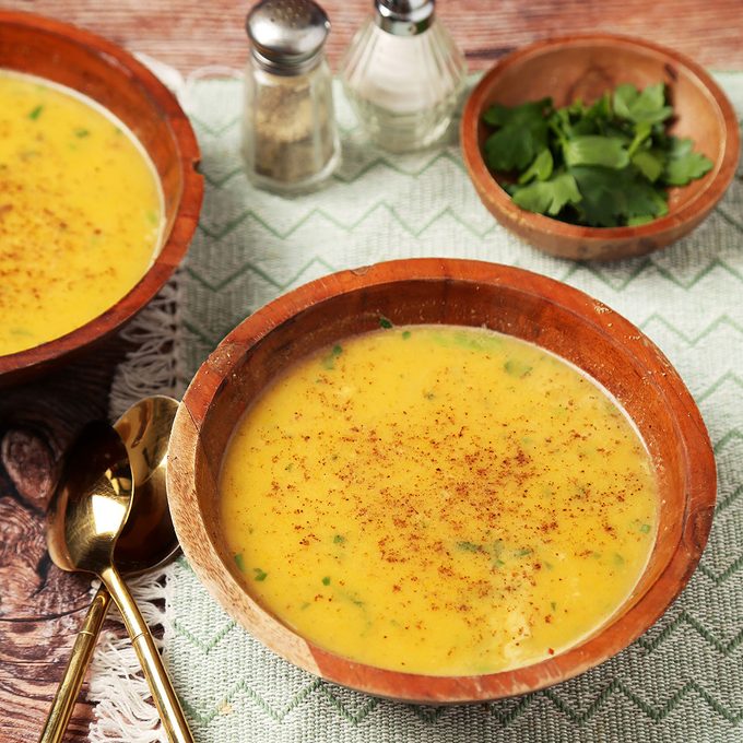Close up of Taste of Home's Chicken Pumpkin Soup served in wooden bowls on a brown wooden surface.