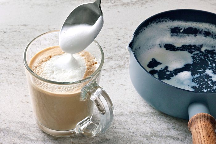 A glass of latte with a spoon of frothed milk being poured into it