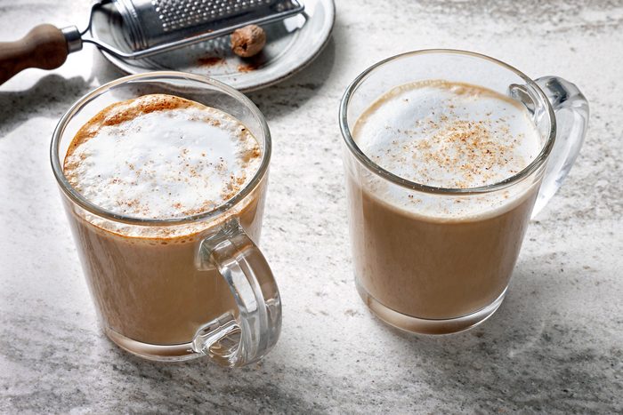 Two glass mugs filled with coffee and a sprinkle of nutmeg on top of the foam sit on a white countertop