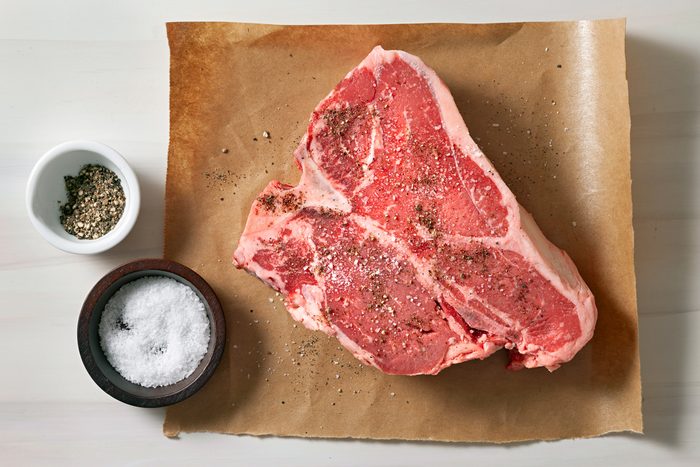 Salt and pepper are being sprinkled over the steak for seasoning.