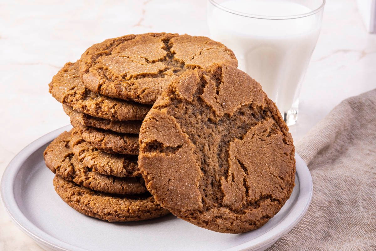 Gingersnap Cookies stacked on white plate on marble surface with milk in the background
