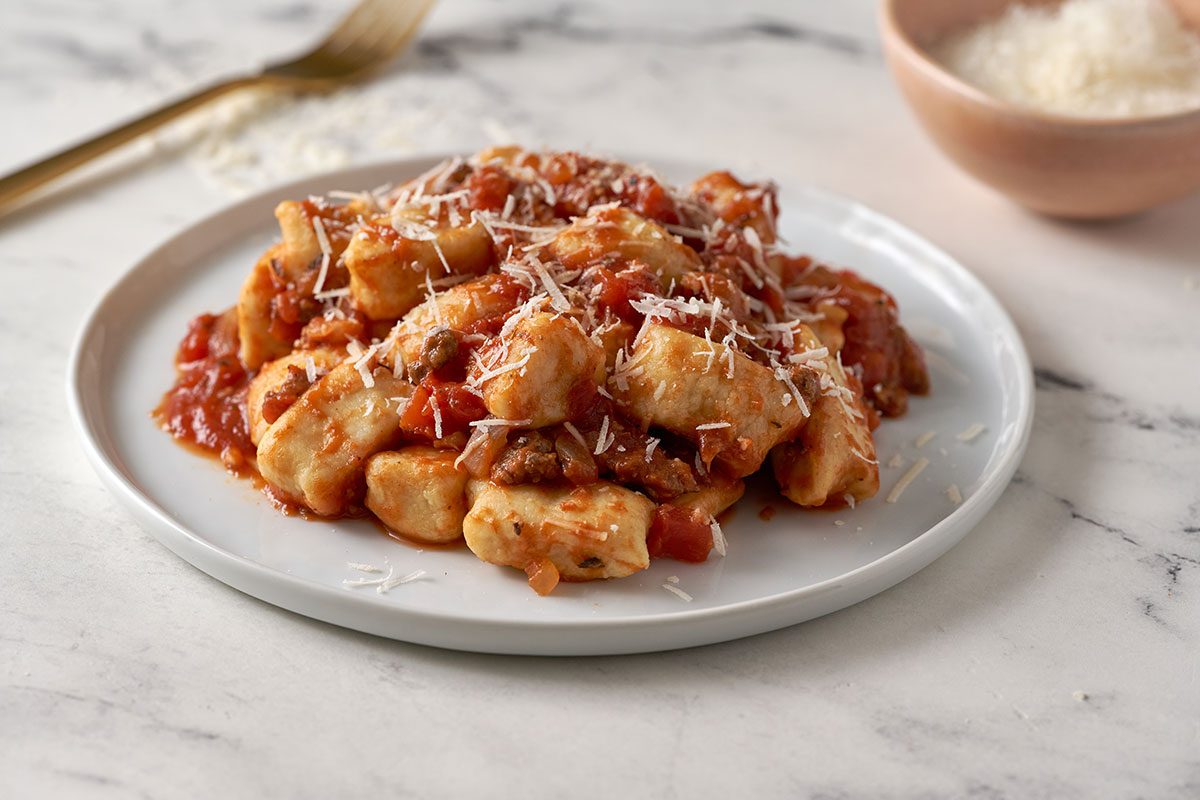 A close-up shot of the Gnocchi Bolognese, highlighting the tender gnocchi and rich beef tomato sauce with melted Parmesan on top, by Taste of Home. Description: A close-up shot of the Gnocchi Bolognese, highlighting the tender gnocchi and rich beef tomato sauce with melted Parmesan on top, by Taste of Home.