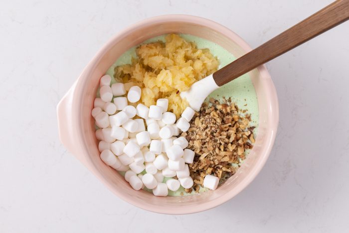 Crushed pineapple, miniature marshmallows and chopped walnuts being combined with gelatin mixture.